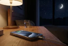 Un iPhone posé sur une table de chevet la nuit, branché à son chargeur, avec l'écran affichant l'indicateur de batterie à 80% et une lune stylisée en arrière-plan. Charger son iPhone la nuit abîme-t-il la batterie ?